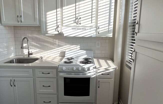 A white kitchen with a stove, sink, and cabinets.