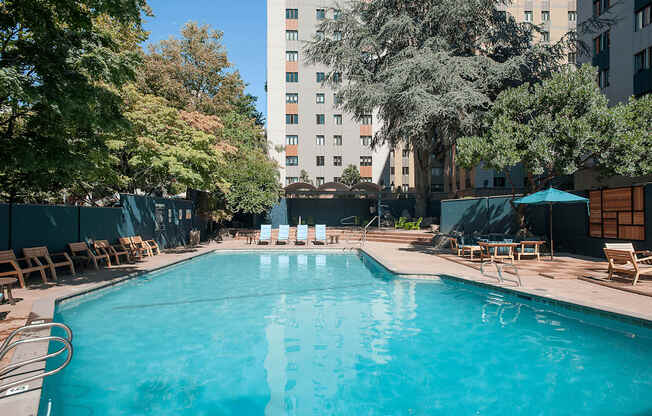 A swimming pool surrounded by trees and chairs.