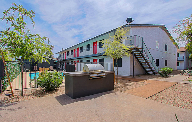 a backyard with a grill and a pool in front of a white building with red and green