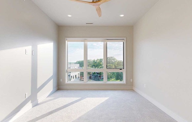 A carpeted bedroom with a floor-to-ceiling 3-panel window, and a ceiling fan.