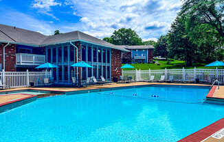 A large swimming pool in front of a house with a deck and umbrellas.