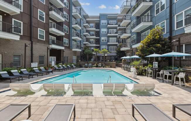 an outdoor swimming pool with lounge chairs and umbrellas in front of an apartment building