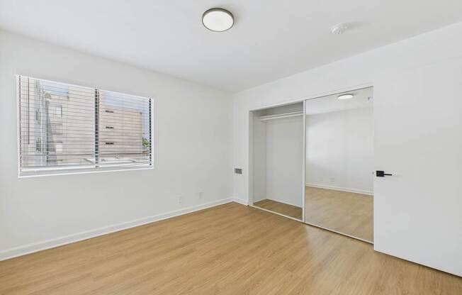 A room with a wooden floor and a window with blinds.
