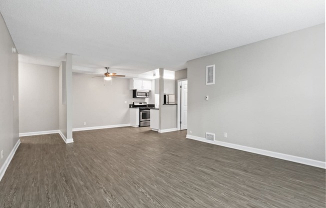 the living room and kitchen of an apartment with wood flooring and a ceiling fan