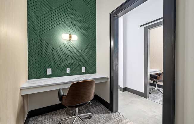 a room with a desk and a chair in front of a wall with green wallpaper