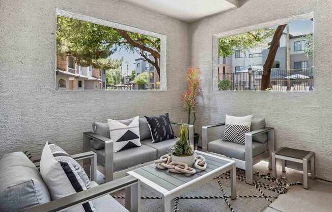 A modern outdoor patio with a glass table and grey couches. at Lazo Apartment Homes, Arizona