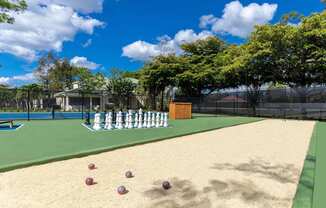 A chess set is set up on a chessboard on a sandy area.