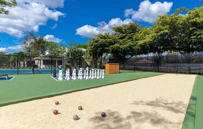A chess set is set up on a chessboard on a sandy area.