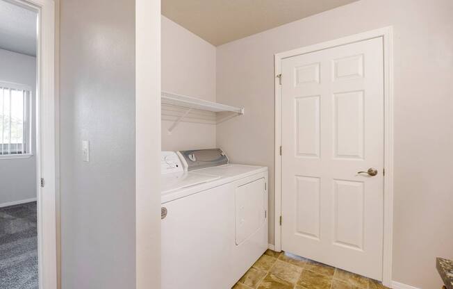 A white laundry machine sits in a small room with a door and a window.