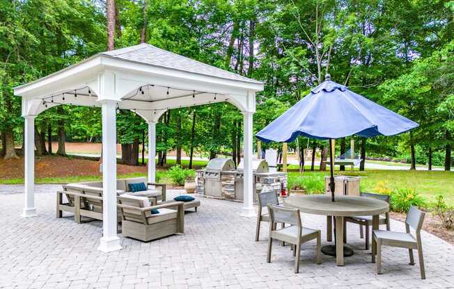 A white gazebo with a blue umbrella is surrounded by chairs and a table.