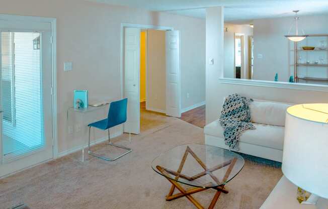 View of living room with a white couch, glass coffee table, and desk at Chisholm Place Apartments in Plano, TX