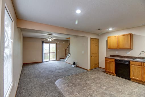 an empty living room with a kitchen and a door to a balcony