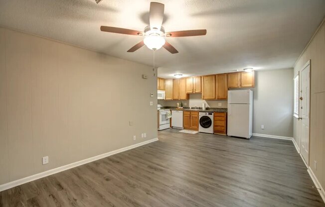 a living room with a ceiling fan and a kitchen in the background