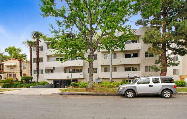 A silver car is parked in front of a white apartment building.