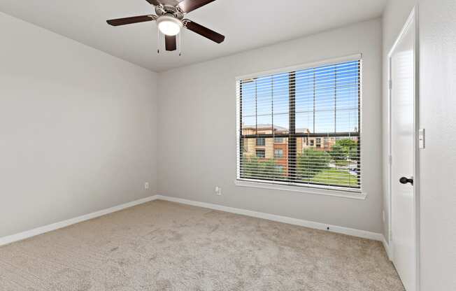 an empty bedroom with a large window and a ceiling fan