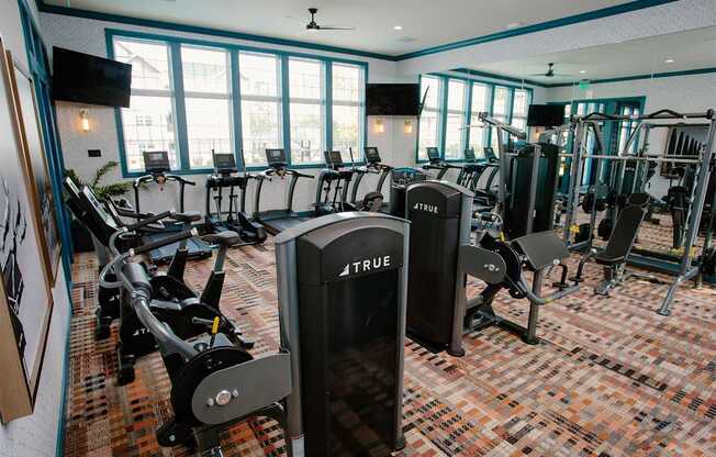 a gym with cardio equipment and weights in a room with windows