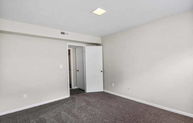 a bedroom with white walls and carpet and a door to a closet