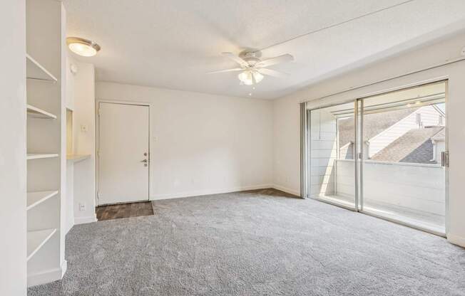 A room with a grey carpet and a ceiling fan.