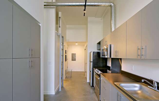 Hallway with concrete floors and at 19th & Mercer, Seattle, WA 98112cabinets on the left and kitchen on the right. A latter on the left side accessing a loft.