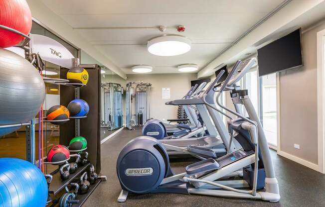 A gym with a row of treadmills and exercise balls.