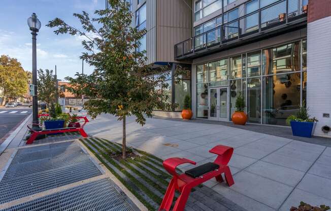 a tree and two red benches on a sidewalk in front of a building at The Shay, District of Columbia