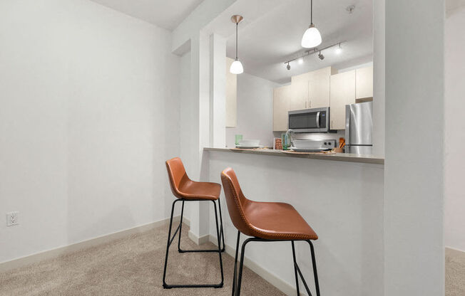 a kitchen with two stools in front of a bar with two chairs