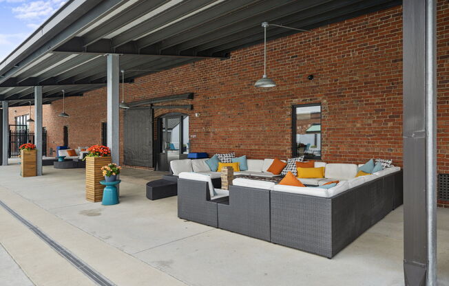 a patio with couches and colorful pillows in front of a brick building