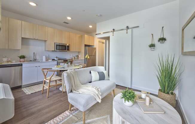 Open floor plan in a stylish living and kitchen area at The Mint Rahway, with light wood cabinets, modern appliances, and a cozy dining setup, ideal for luxury apartment rentals near the Union County Performing Arts Center.