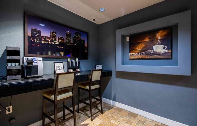 a bar with stools and a coffee machine with a large screen on the wall behind it At Metropolitan Apartments in Little Rock, AR