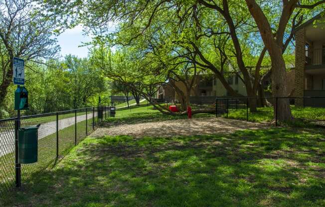 A fenced in dog park with trees at Chisholm Place Apartments in Plano, TX