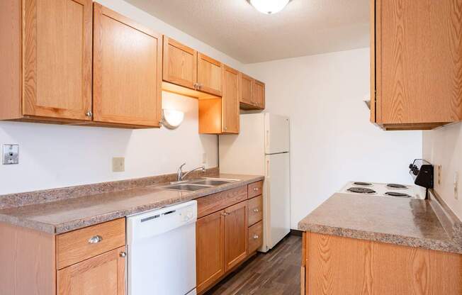A kitchen with wooden cabinets and a white dishwasher. West Fargo, ND Saddlebrook Apartments