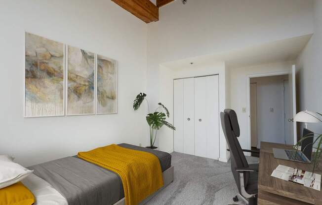 a bedroom with a bed with a yellow blanket and a desk at Lowertown Commons Apartments, St. Paul