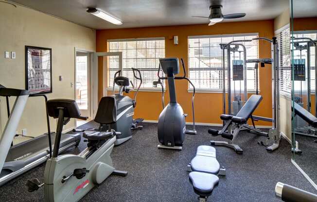 a gym with cardio equipment and weights with orange walls at 2000 Lake Washington Apartments, Washington