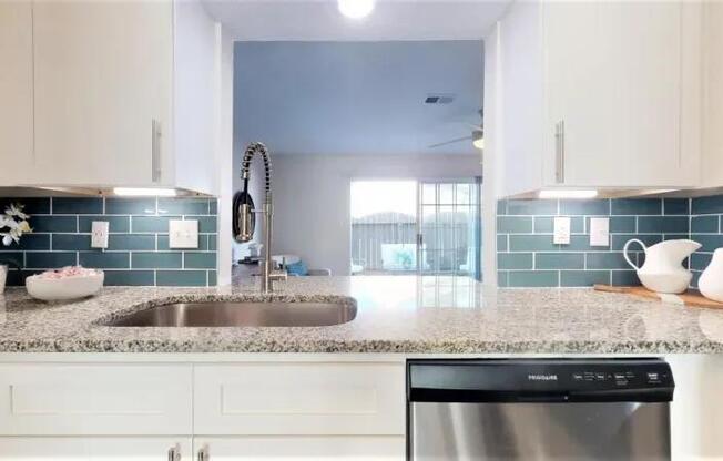 A kitchen with a stainless steel dishwasher and white cabinets.