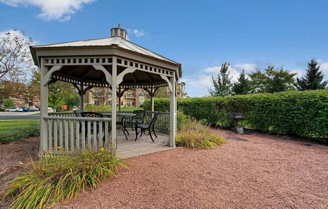 A charming outdoor gazebo here at Swan Creek with shaded seating, landscaped greenery, nearby grill area, and peaceful surroundings, creating a relaxing, welcoming community retreat.