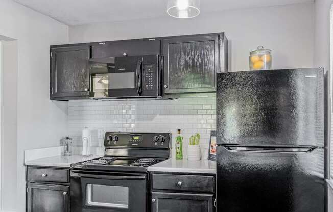 A black fridge stands in a kitchen with black appliances and white countertops.