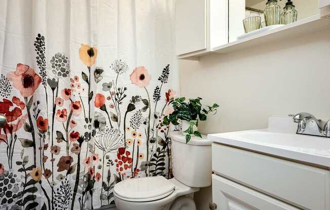 A white toilet sits next to a sink in a bathroom with a floral shower curtain.