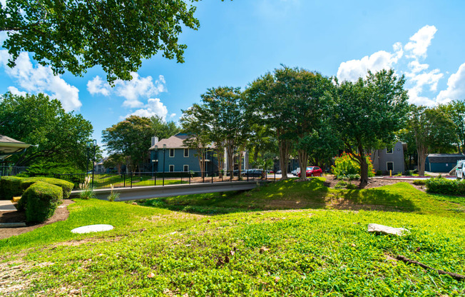 a park with green grass and trees and houses in the background