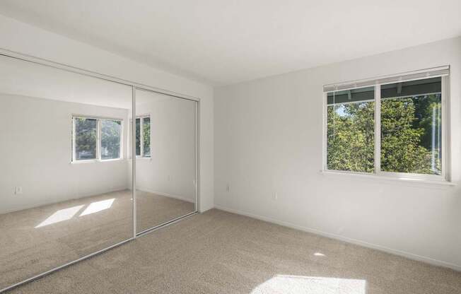 A room with a carpeted floor and a window showing trees outside at Clackamas Trails Apartments, Oregon, 97222