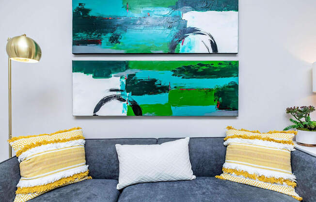 A grey couch with two pillows and a painting on the wall.