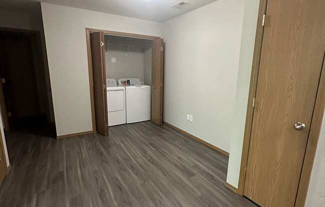 an empty living room with wood flooring and a door to a kitchen