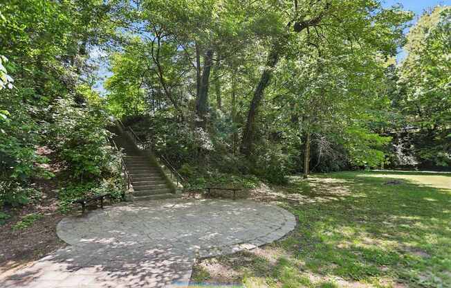 A circular stone pathway leads up a staircase in a lush green park.