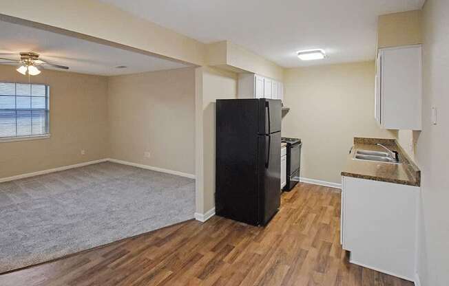 A kitchen area with a black refrigerator and wooden flooring.