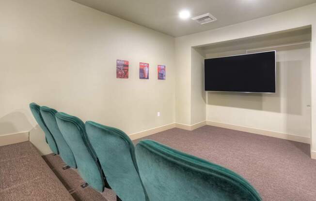 A room with a row of green chairs and a black screen on the wall.