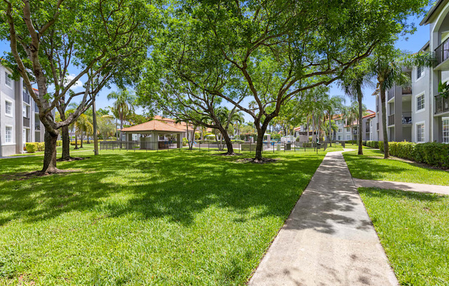 A tree-lined walkway in a park with a gazebo in the distance.