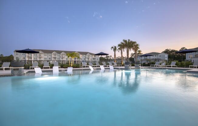 a large swimming pool with white chairs in front of a resort