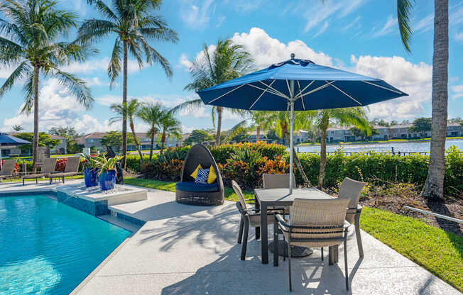 A poolside area with a table and chairs under an umbrella.