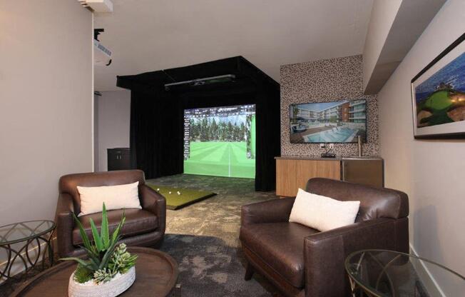 a living room with two leather chairs and a view of a golf simulator