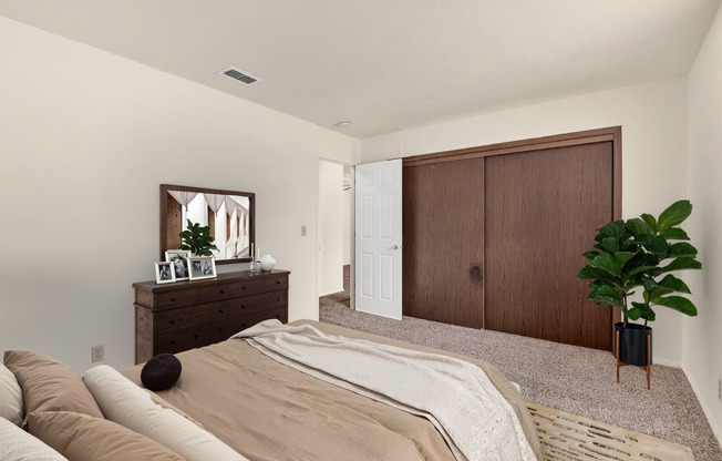 A bedroom with a bed, dresser, mirror, and plant.