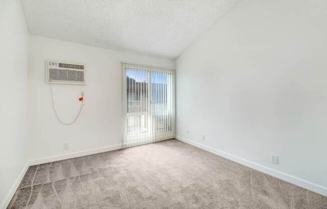 A room with a window covered by blinds and a wall-mounted air conditioner unit.